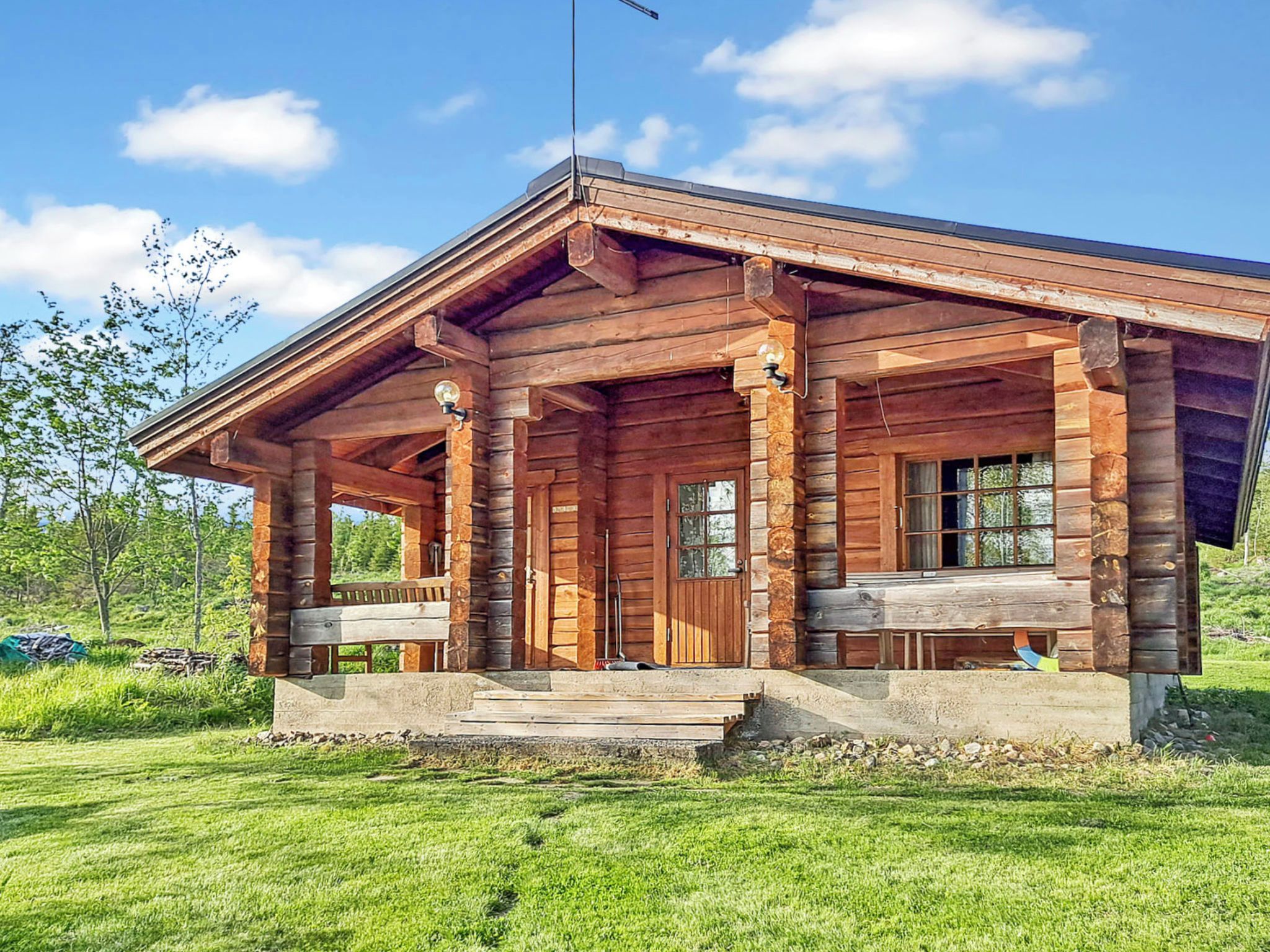 Une cabane en bois avec une véranda, de grandes fenêtres et une cheminée.