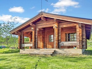 A wooden cabin with a porch, large windows, and a chimney.