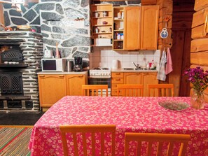 A cozy kitchen with wooden cabinets, a stone wall, a microwave, a stove, and a dining table with chairs. - Honkakoti by Interhome (Kuopio)