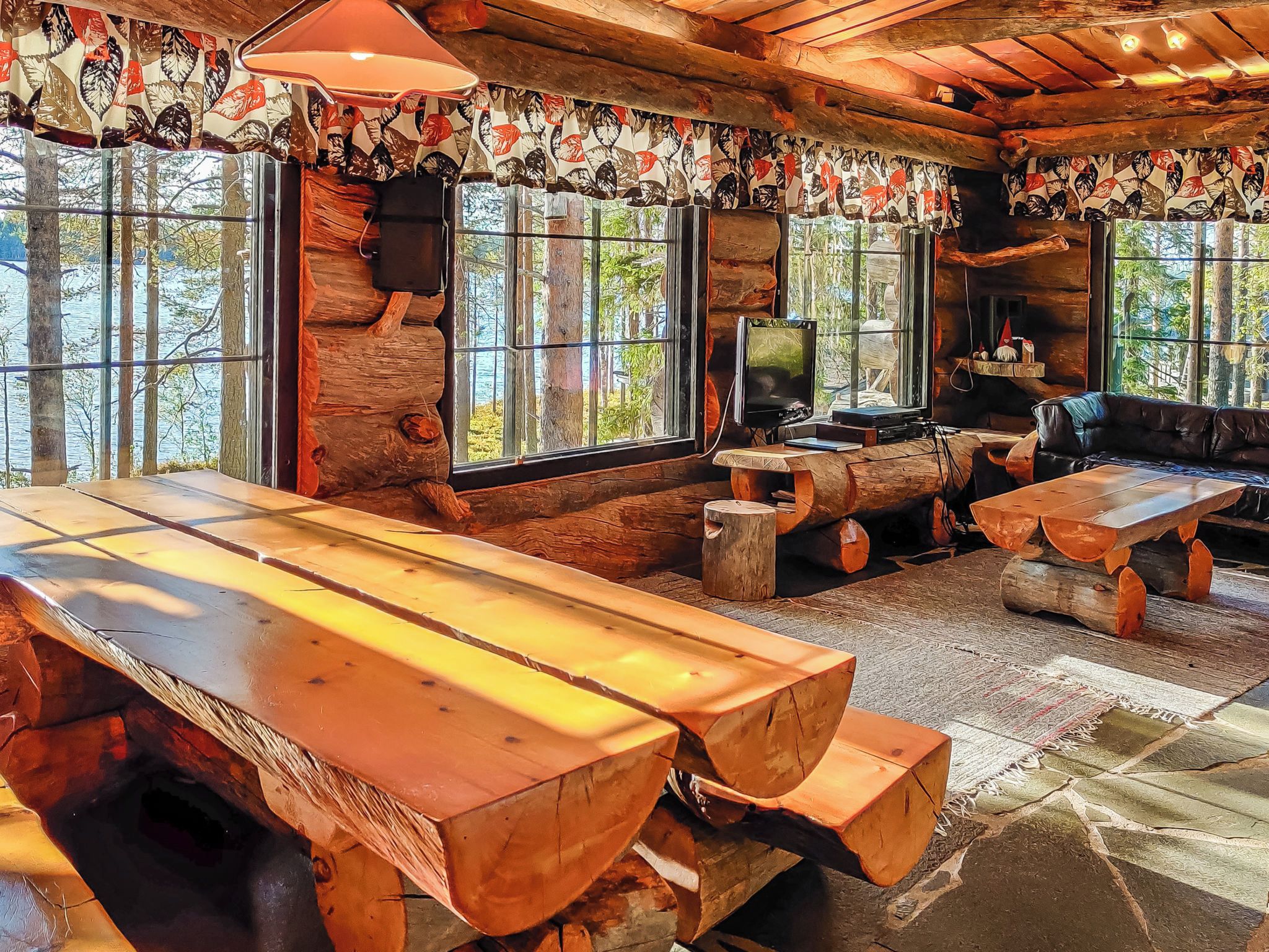 Ein rustikales Blockhaus-Interieur mit einem großen Holztisch, einem Fernseher und einem Sofa.