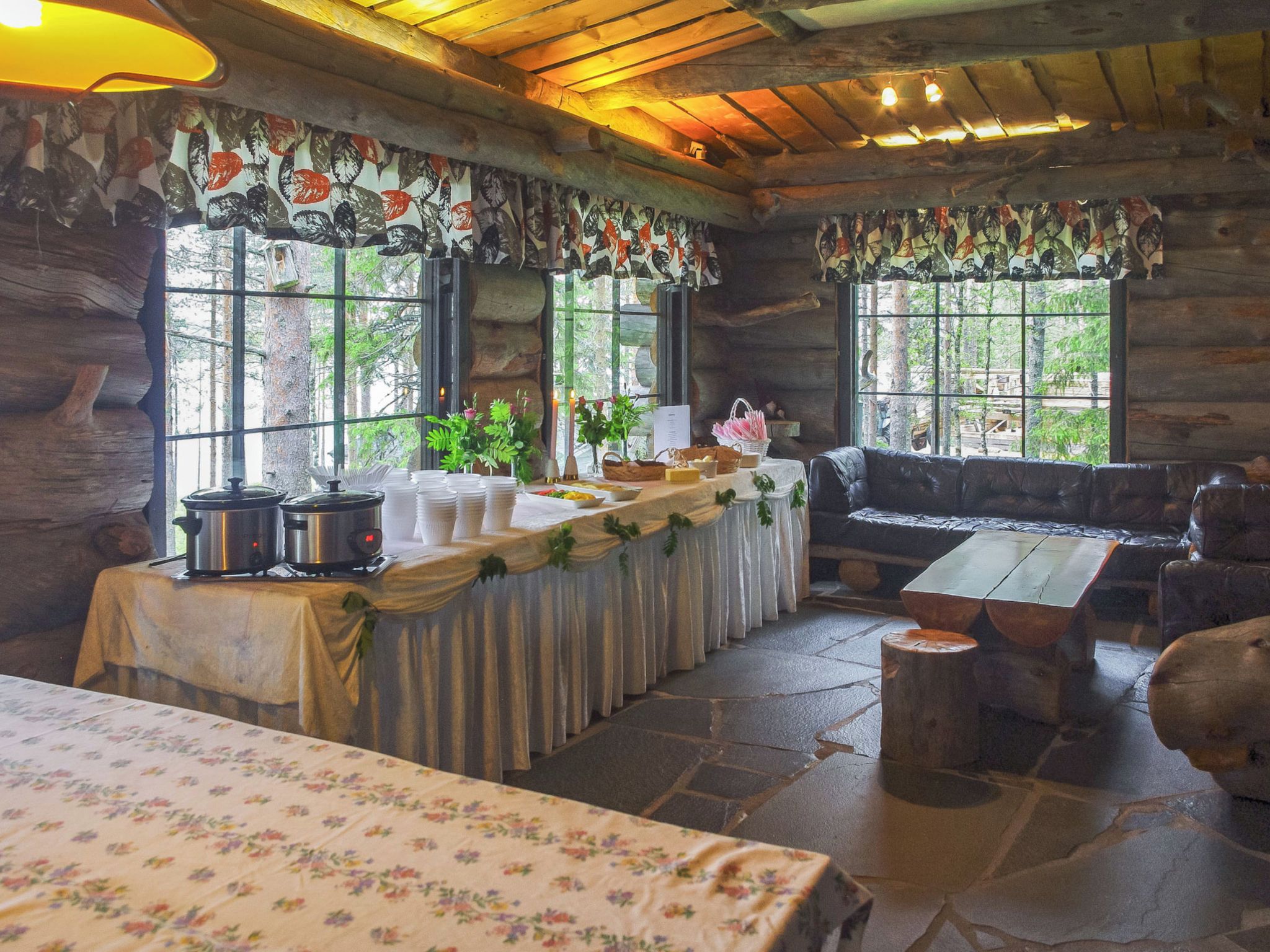 A rustic cabin interior with a dining area, a sofa, and a table set for a meal.