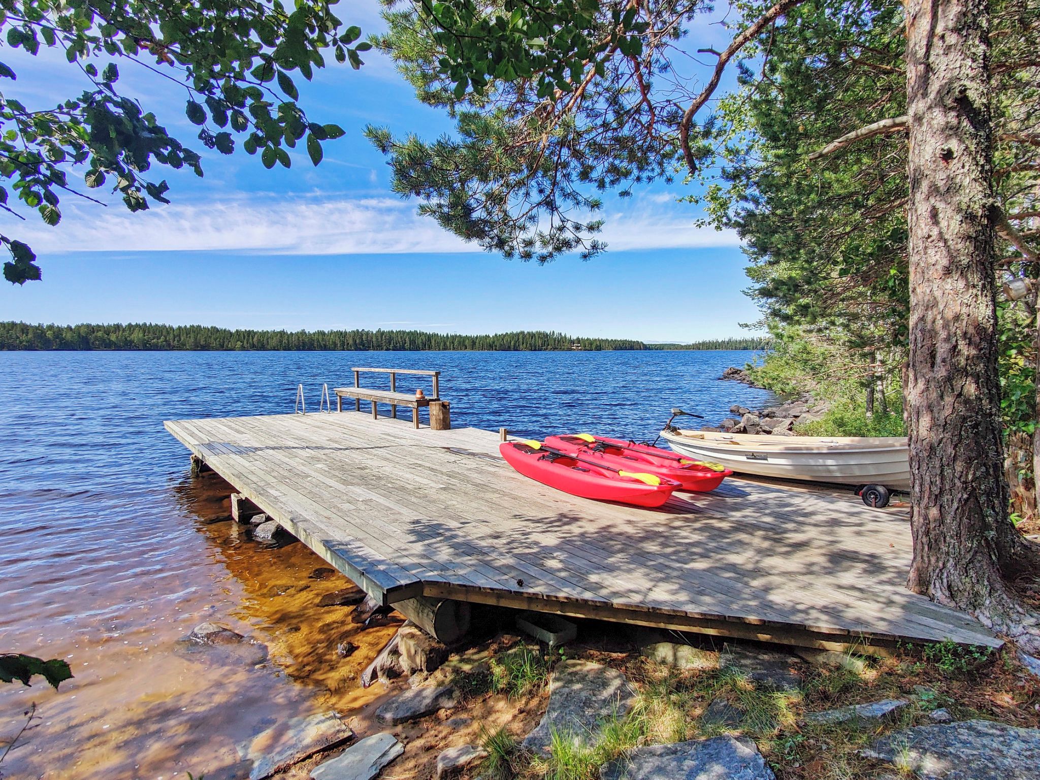 A wooden dock extending into a calm lake with kayaks and a small boat docked at the end.