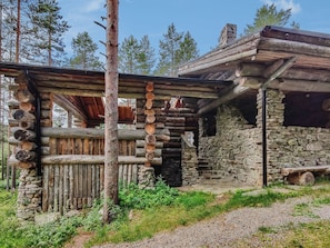 A rustic cabin with a stone foundation and wooden log construction, surrounded by a natural forest setting.