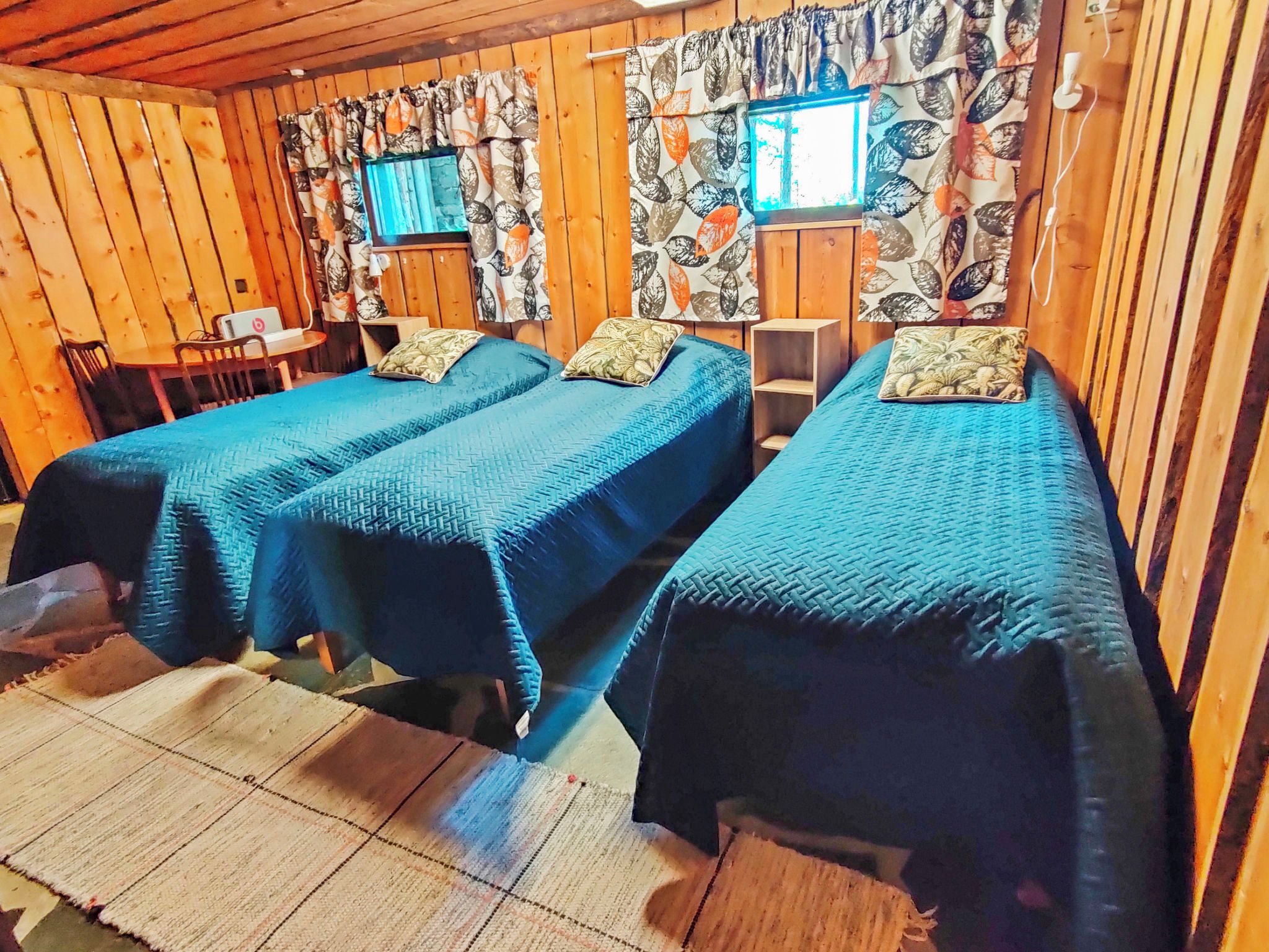 Quarto com duas camas, uma escrivaninha com computador e uma janela com cortinas.