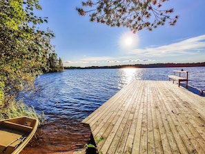 A wooden dock extending into a calm body of water, with a boat docked at the end and a forested shoreline in the background. - Puuhamaa by Interhome (Rovaniemi)