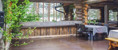 A rustic wooden interior with a stone wall, wooden ceiling beams, and a dining area with tables and chairs.