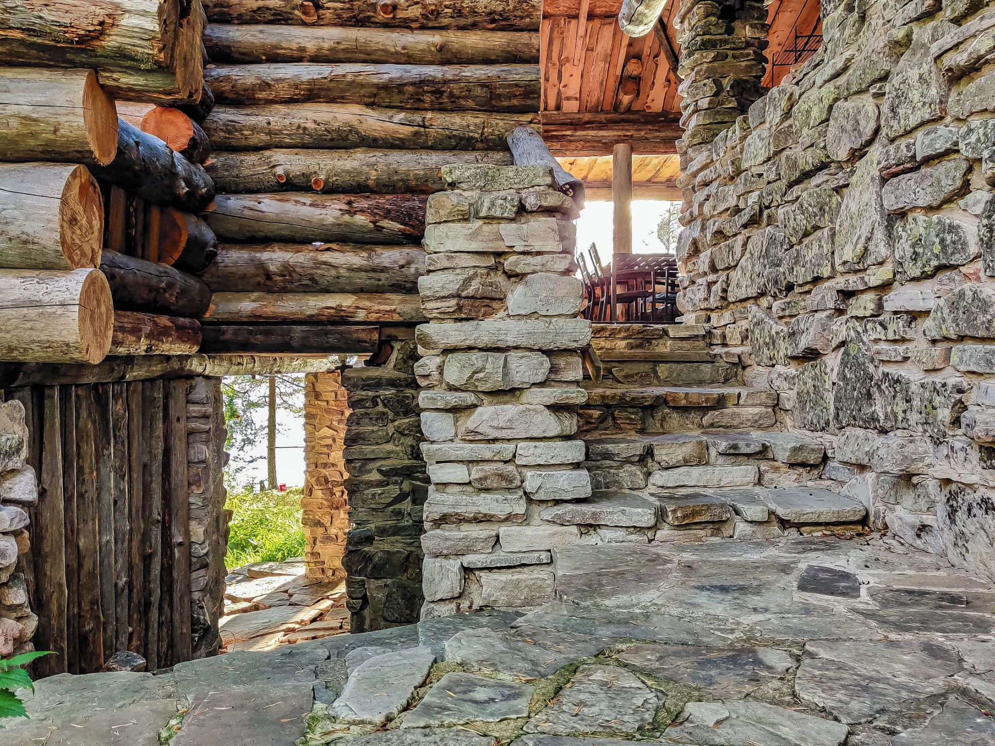 Un bâtiment rustique en pierre, doté d’une porte en bois et d’un mur en rondins.