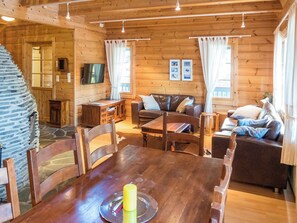 Ein gemütliches Cabin-Interieur mit Esstisch, Holzstühlen, einer Couch und einem an der Wand befestigten Fernseher.