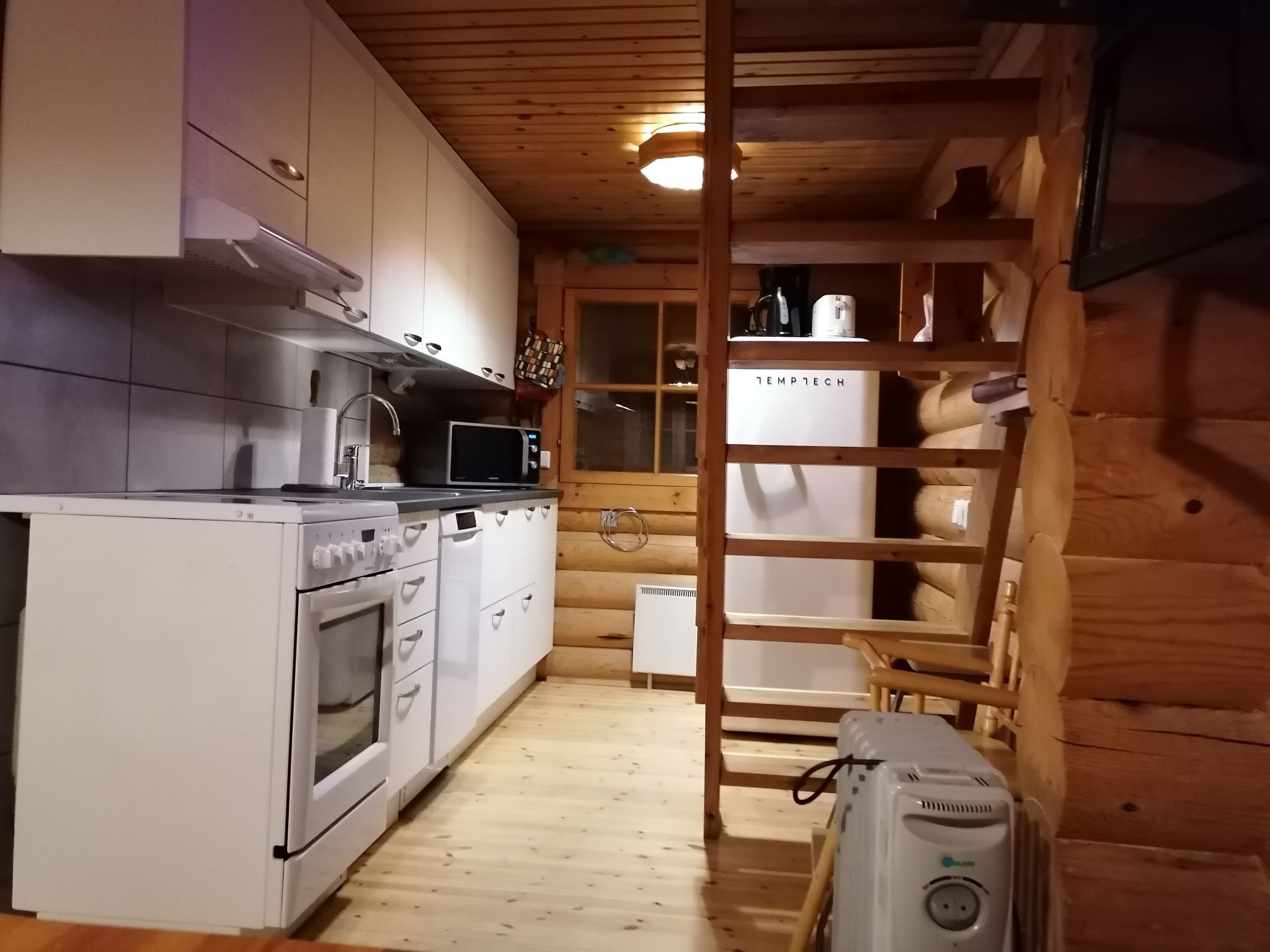 Une cuisine compacte avec des appareils électroménagers blancs, une échelle en bois et une fenêtre donnant sur un beau paysage.