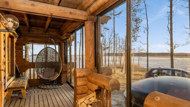 A wooden cabin with a wooden deck, a hanging chair, and a view of a car and trees outside. - Huvilakoti 1 by Interhome (Liperi)