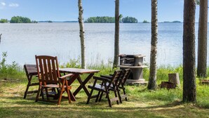 A lakeside picnic area with wooden benches and a grill. - Huvilakoti 1 by Interhome (Liperi)