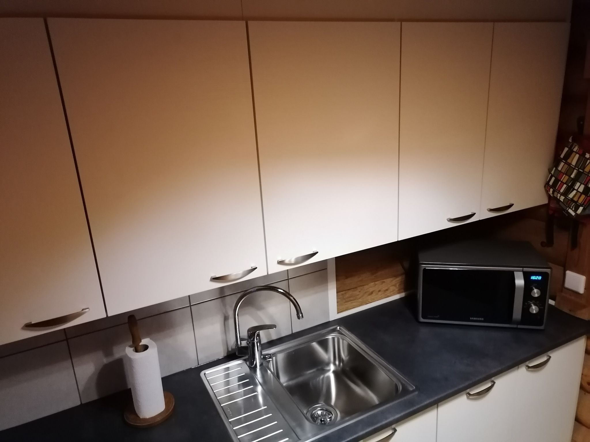Een keuken met witte kastjes, een roestvrijstalen spoelbak, een magnetron en een keukenrol.