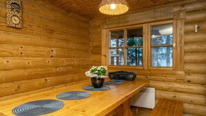 A wooden cabin interior with a long dining table, a hanging light fixture, and a window with a view of trees. - Huvilakoti 1 by Interhome (Liperi)