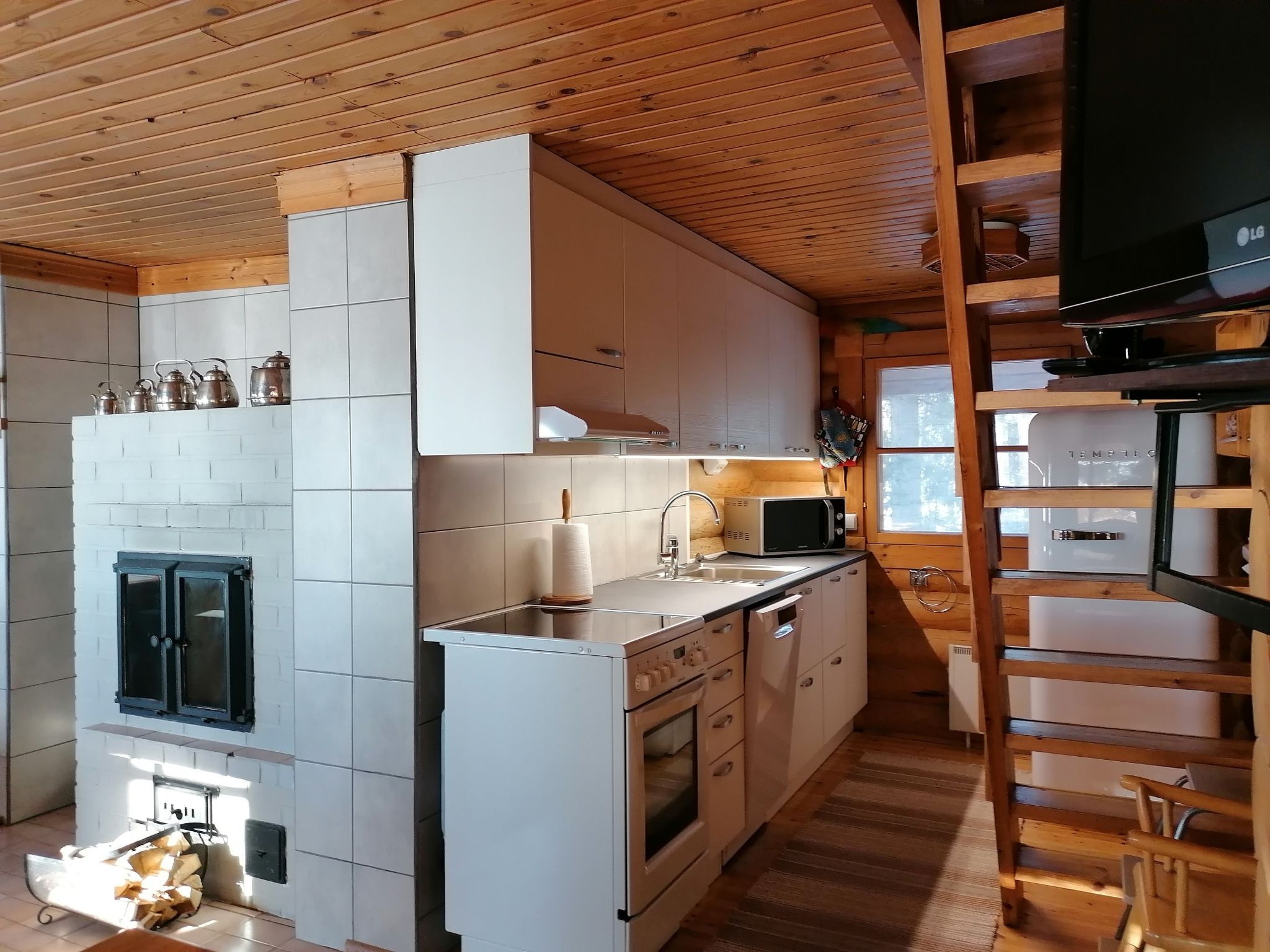 Pieni, käytännöllinen keittiö, jossa on valkoiset kaapit, liesi ja mikroaaltouuni.