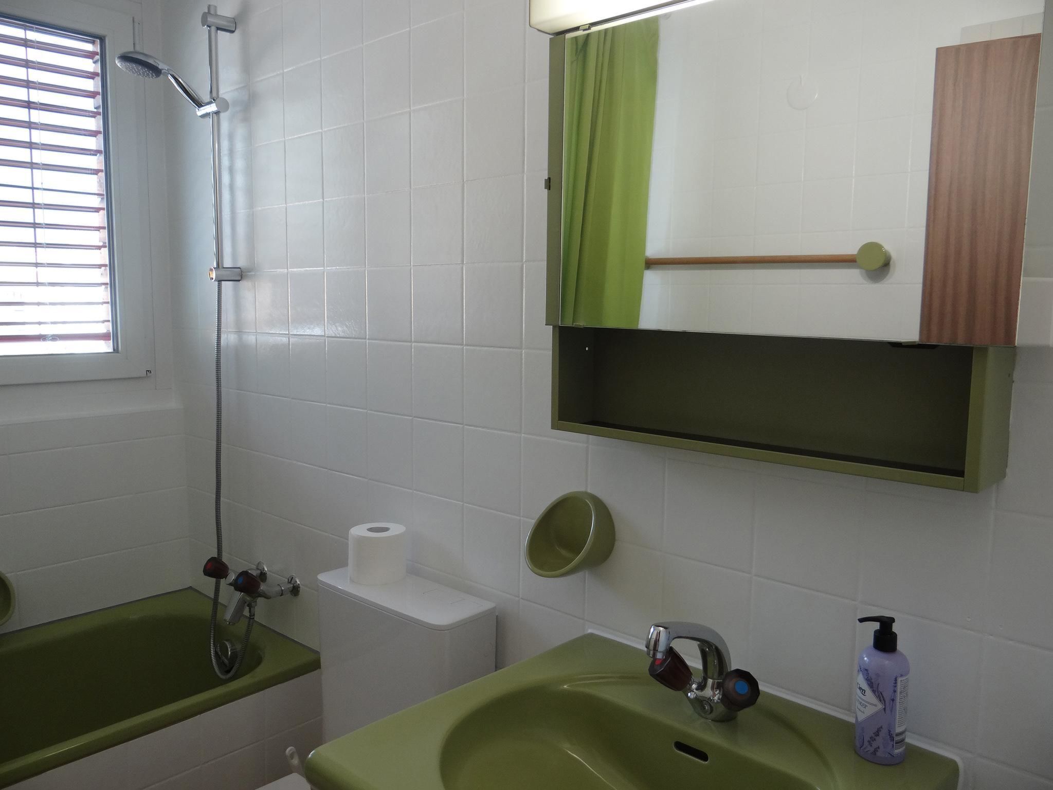 A bathroom with a shower, toilet, sink, and a mirror with a green curtain.
