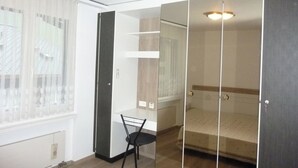 Una habitación con cama, silla, armario y ventana con persianas.
