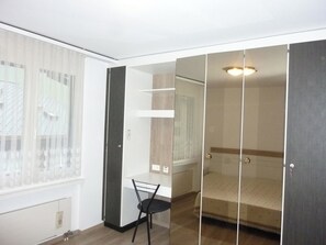 A room with a bed, a chair, a wardrobe, and a window with blinds.
