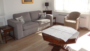 Una sala de estar con un sofá, una mesa de centro de madera, una silla de mimbre, una lámpara de pie y un cuadro en la pared.