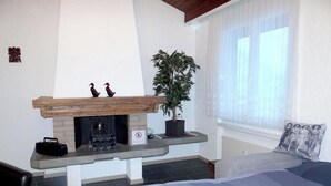 Une chambre avec une cheminée, un lit, une fenêtre avec des rideaux légers et une plante en pot.