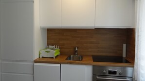 Une cuisine compacte avec des meubles blancs, un plan de travail en bois, un évier, un lave-vaisselle et un four.
