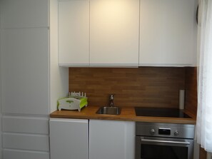 Cocina compacta con armarios blancos, encimera de madera, un lavamanos, lavavajillas y horno.