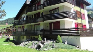 Hotel de varios pisos con balcones, un jardín y montañas al fondo.