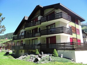 A multi-story hotel with balconies, a garden area, and a mountainous backdrop.