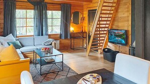 Interior acogedor de una cabaña con sofá, mesa de centro, televisor y una escalera que lleva a una zona superior.