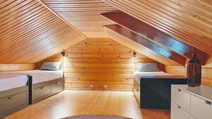 Un dormitorio acogedor en el ático con paredes de madera, una cama litera, un escritorio y un mueble pequeño.