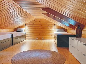 Une chambre située dans un espace de type « loft », avec un plafond en pente, des murs en bois, deux lits, une commode et un tapis.
