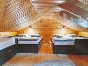 A small attic bedroom with two beds, wooden walls, and a sloped ceiling. - Uolevintie 39b by Interhome (Kuusamo)