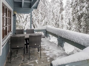Un espace extérieur aménagé avec des meubles de jardin en osier et une table, le tout abrité, et entouré d’arbres couverts de neige.