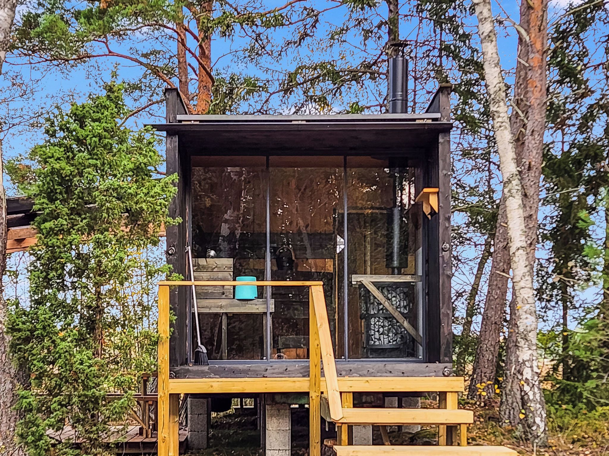 En stuga byggd av trä med en glasfasad, en trätrappa och en skorsten.