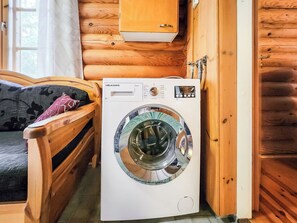 Een kleine kamer met houten inrichting, een wasmachine, een bank en een raam.