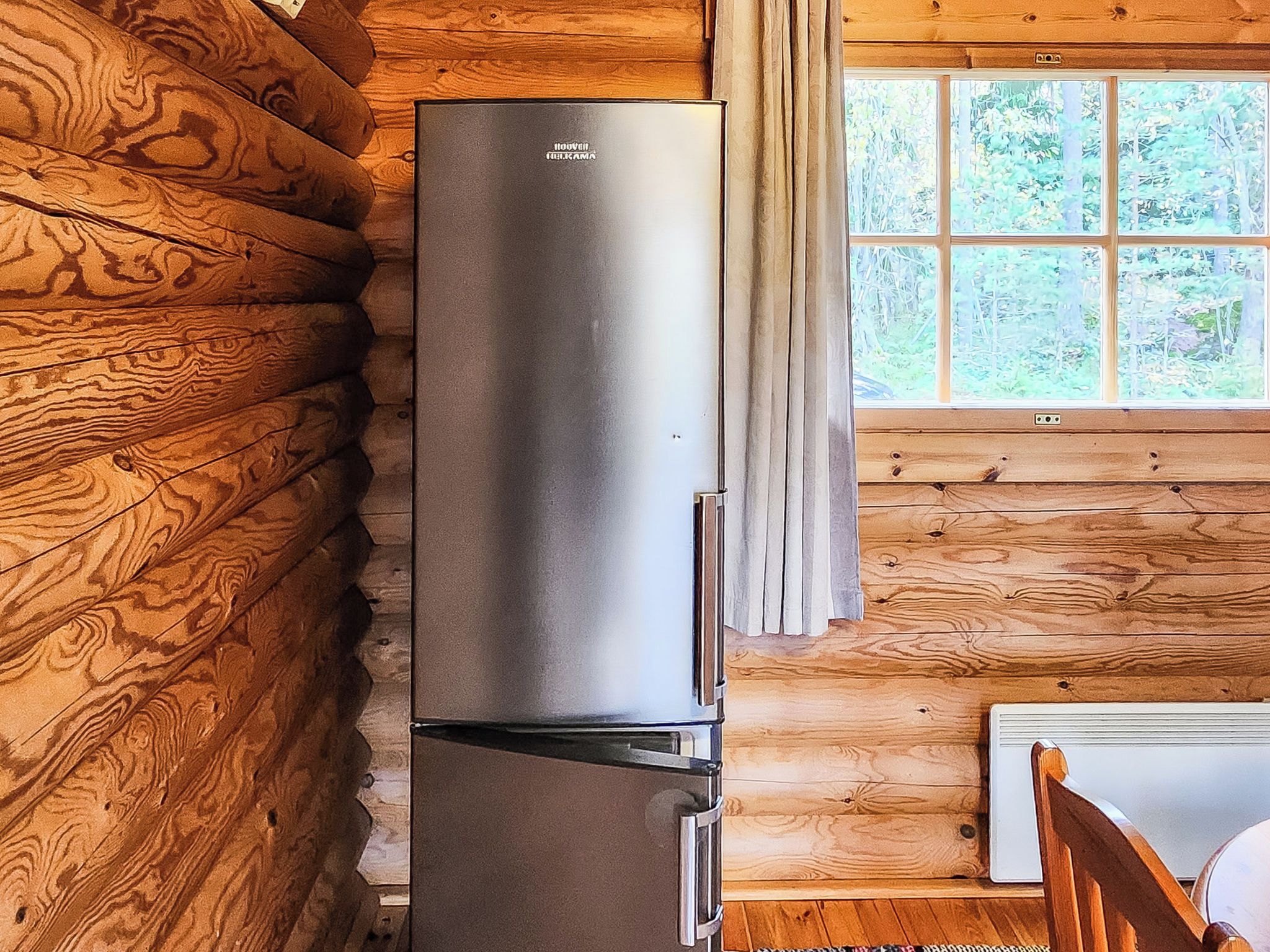 Cocina compacta y moderna con refrigerador de acero inoxidable integrado, paredes de madera y ventana con vistas a zonas verdes.
