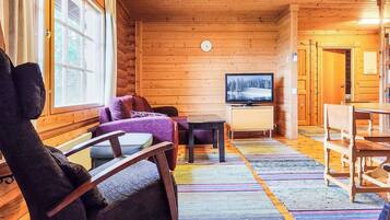 L'intérieur d'une cabane en rondins, avec un plafond en bois, un téléviseur, un canapé, un fauteuil et une table à manger.