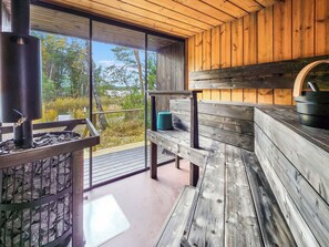 A wooden cabin with a stone fireplace, a bench, and a view of the outdoors.