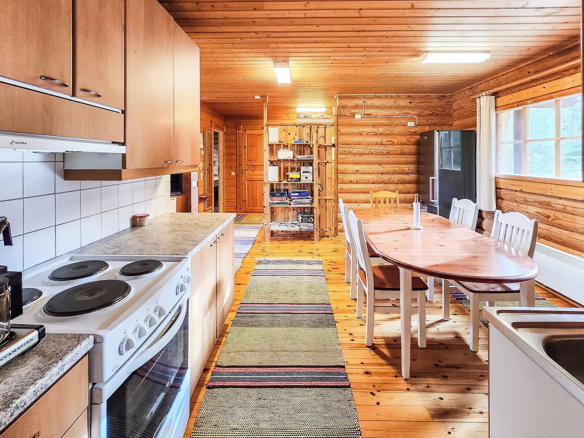 Interno di una baita di legno con angolo cottura, zona pranzo e una libreria.