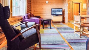 L’intérieur d’un chalet confortable, avec un canapé, un fauteuil, une télévision et un coin repas.