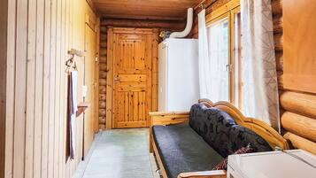 Un pasillo estrecho con paredes de madera, un banco, un refrigerador blanco y una ventana con cortinas.