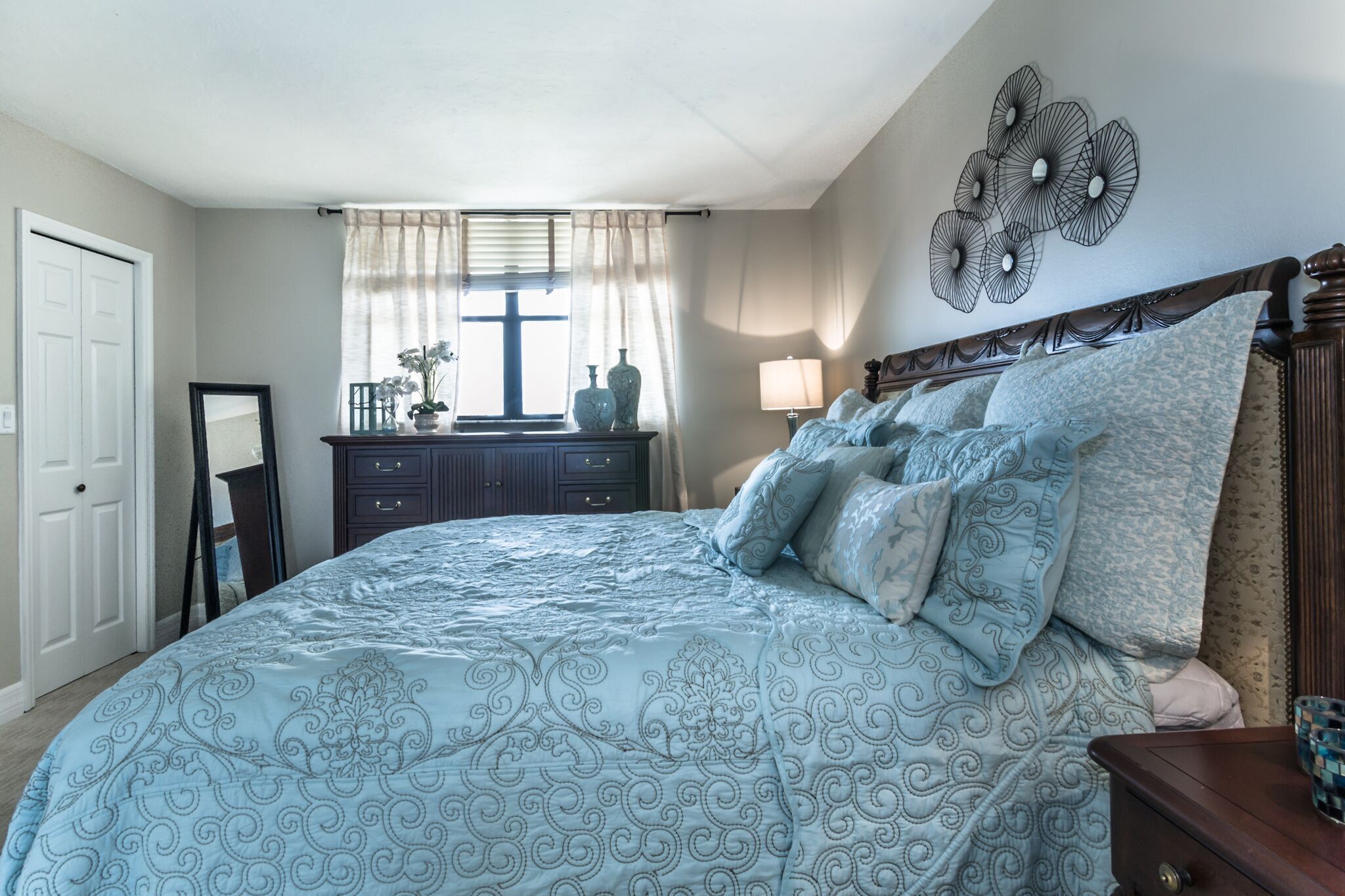 A bedroom with a large bed, a dresser, a mirror, a lamp, and a wall decoration.