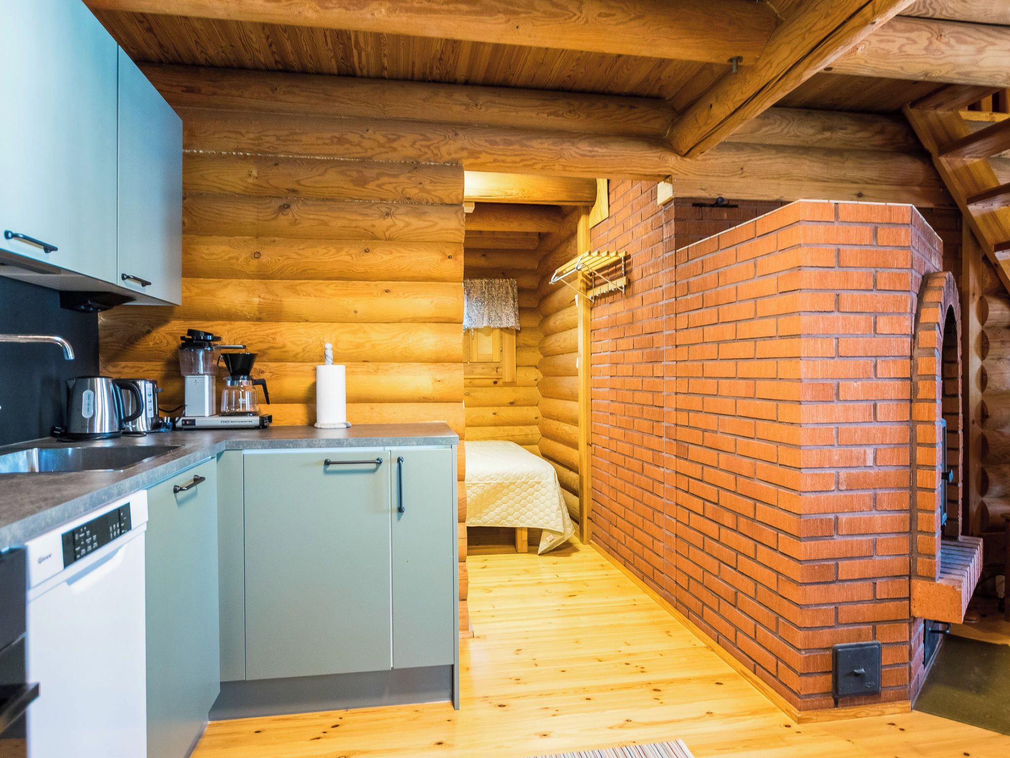 Uma cabana rústica e compacta com cozinha compacta, uma cama e lareira de tijolos.