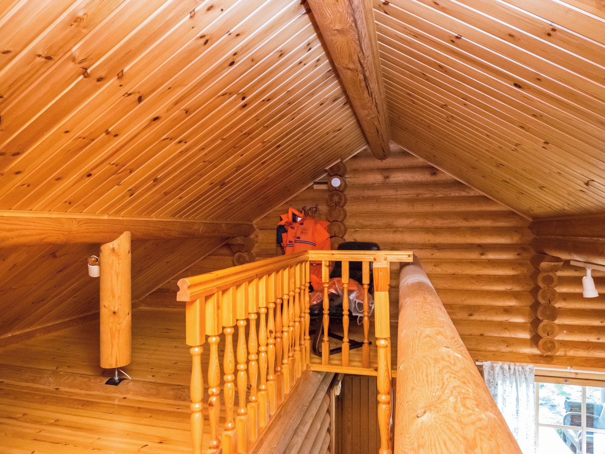 Interior de madera con una escalera de madera y una pared de troncos.