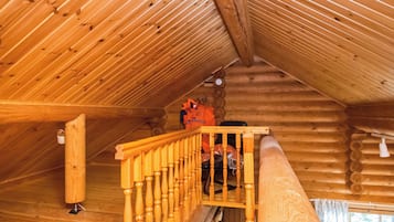 Interior de madera con una escalera de madera y una pared de troncos.