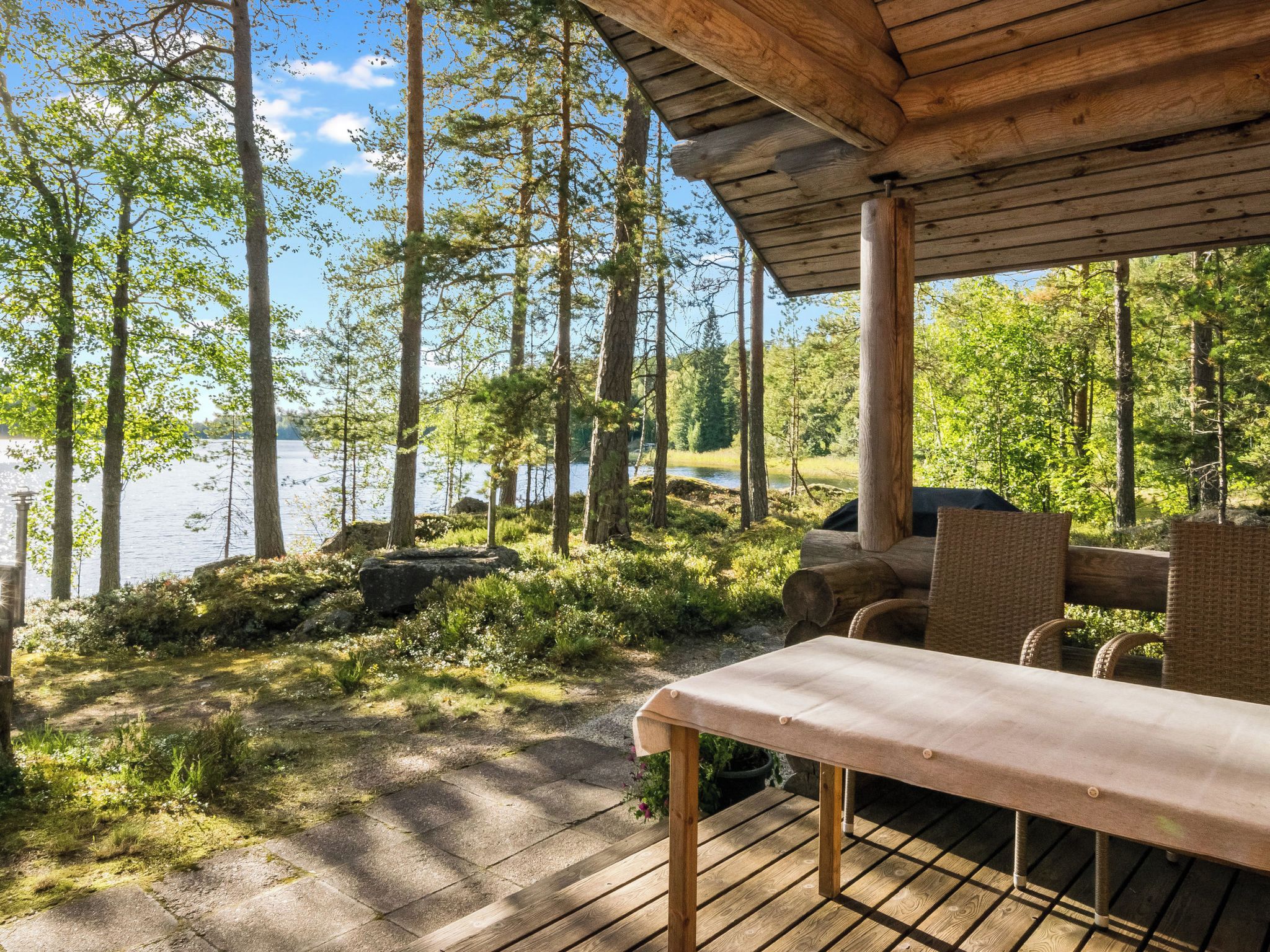 Um deck de madeira com mesa e cadeiras, com vista para um lago rodeado por árvores.