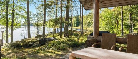 Eine Holzterrasse mit Tisch und Stühlen, mit Blick auf einen von Bäumen gesäumten See.