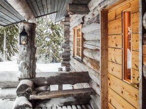A log cabin with a wooden staircase leading to a door, a lantern hanging from a tree, and snow-covered ground.