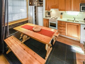 Een praktische keuken met houten kastjes, een fornuis, een spoelbak en een eettafel met bankjes.