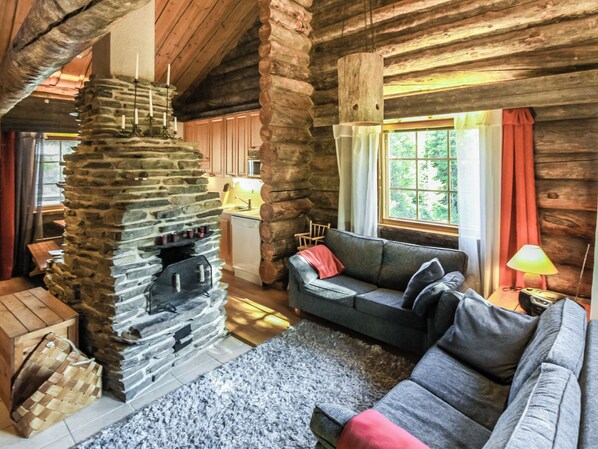 A cozy log cabin interior with a stone fireplace, a sofa, and a window with curtains.