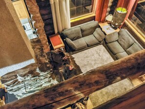 A room with a stone wall, a gray sectional sofa, a wooden coffee table, and a hanging lamp.